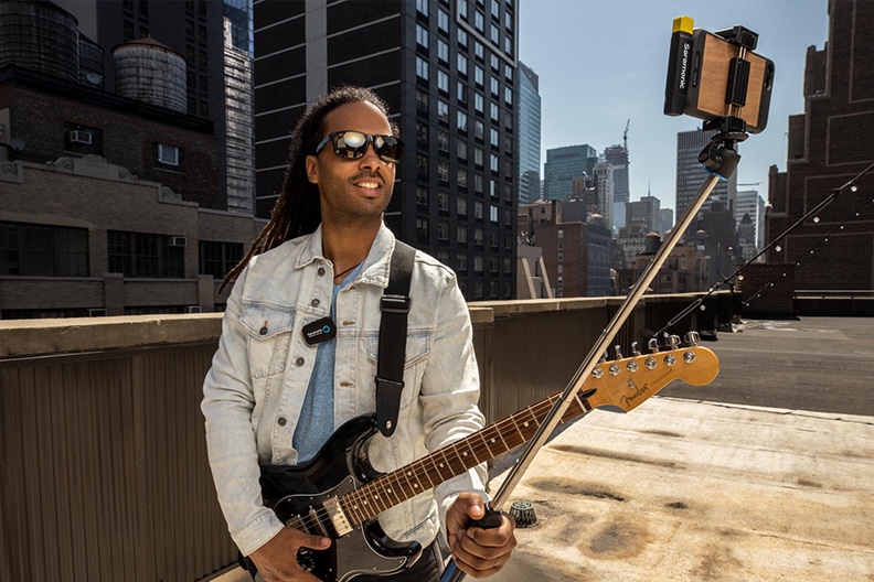 Gitarrenspielender Mann mit einem Selfie-Stick inkl. Smartphone und Saramonic Mikrofon