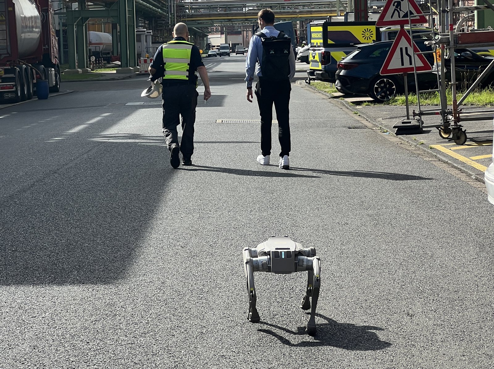 Legged robot following two staff members along a road in an industrial park