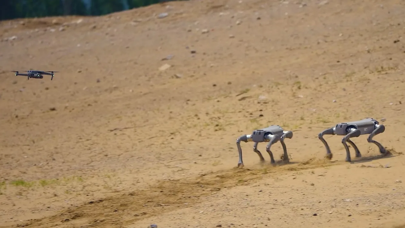 Two legged robots and a drone operating on sandy terrain