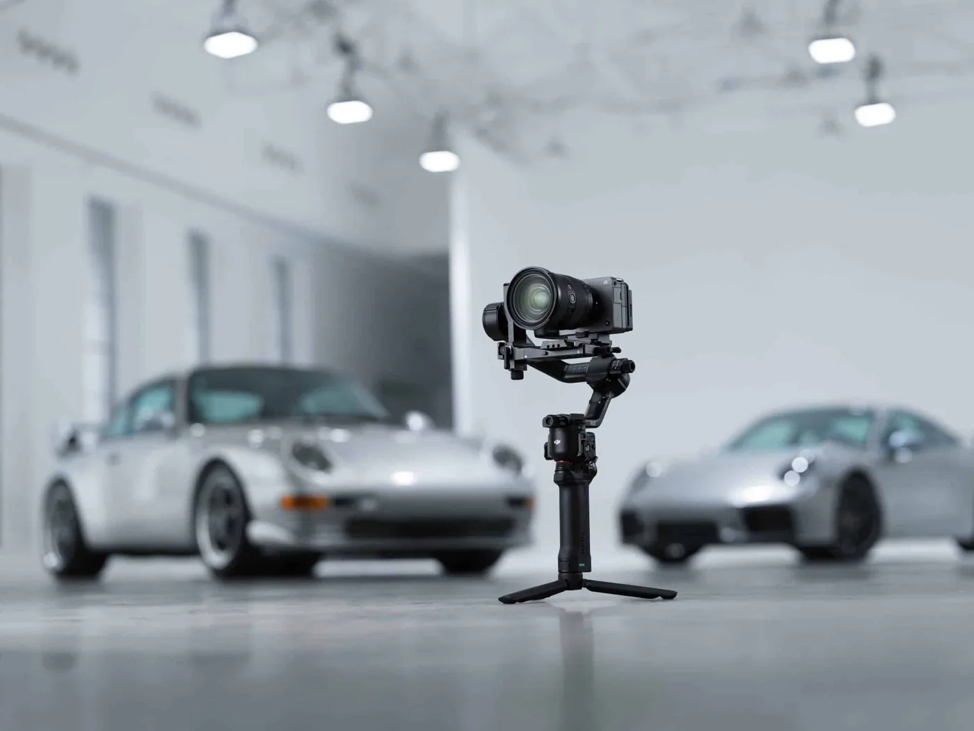 DJI RS gimbal with a camera on a tripod in front of two sports cars