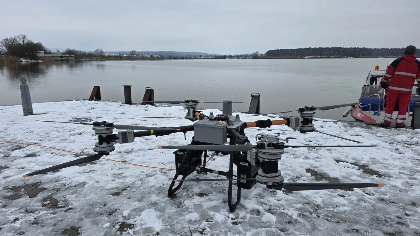 DJI FlyCart transport drone on the snowy shore of a lake, with Wasserwacht rescuers behind