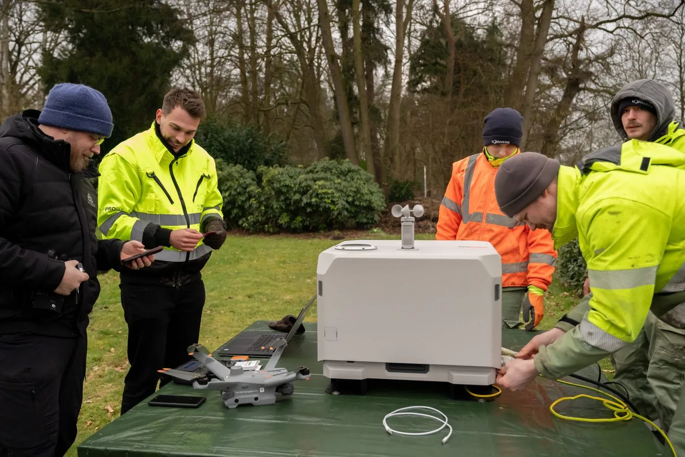 Briefing at a drone dock outdoors, participants in high-visibility jackets