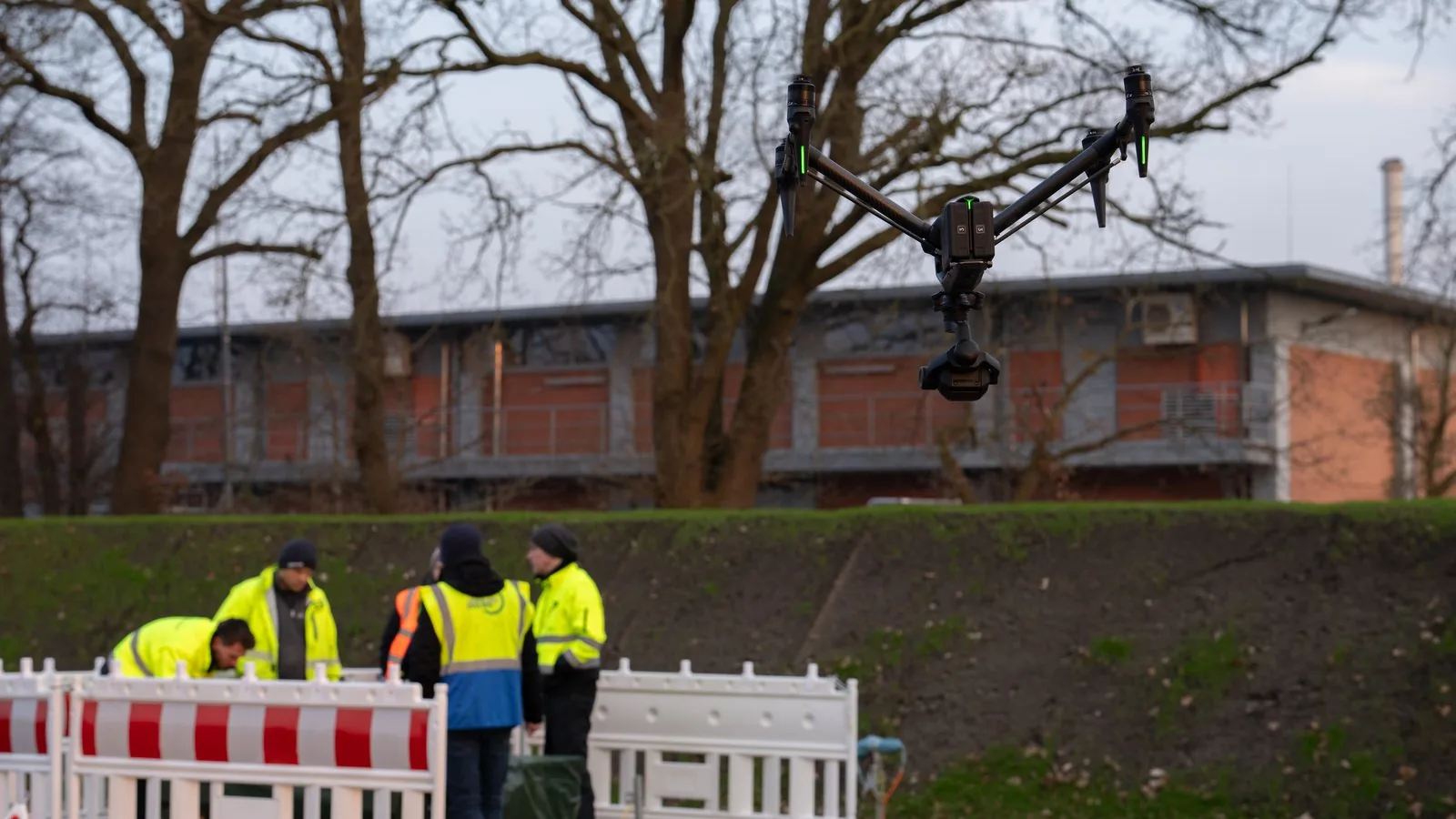 Drone in flight above a work site, with a team working at the barrier behind it